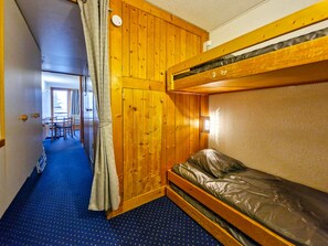 Een kamer met een stapelbed, houten wanden, een gordijn, een klein tafeltje en een stoel.