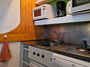 Een keuken met een magnetron, koffiezetapparaat, een roestvrijstalen spoelbak en een fornuis met vier branders.