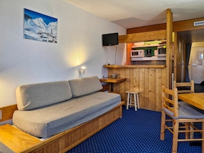 A cozy room with a sofa, a small stool, a wooden table, a microwave, and a television.