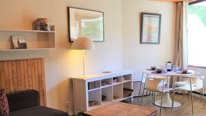 Un salon moderne comprenant un canapé, une table basse, un coin repas avec une table et des chaises, ainsi que des étagères ornées d’objets décoratifs.