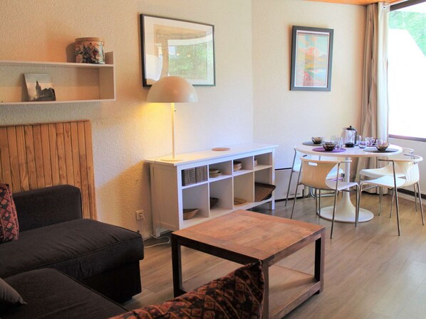 Una sala moderna con un sofá, una mesa de centro, un comedor con mesa y sillas, y estantes con objetos decorativos.