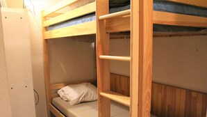 Un lit superposé avec une échelle, un lit simple et une étagère fixée au mur.