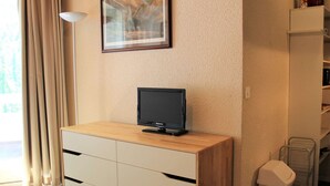 Une pièce avec un meuble en bois, un tableau encadré au mur, un téléviseur posé sur le meuble et une poubelle.