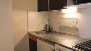 Une cuisine compacte équipée d’un évier en acier inoxydable, d’un four à micro-ondes et d’un four encastré.