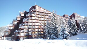 A multi-story hotel with balconies, surrounded by snow-covered trees and a clear sky. - Studio for 4, ski-in/ski-out, Arc 1800 (Les Arcs 1800)
