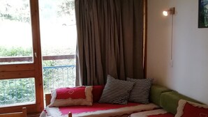A cozy room with a wooden bed, a window with curtains, and a view of greenery outside. - Studio for 4, ski-in/ski-out, Arc 1800 (Les Arcs 1800)