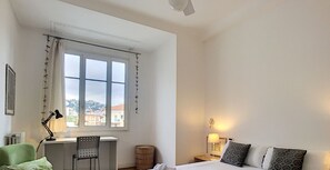 Un dormitorio con una cama grande, un escritorio, una silla y vistas a la ciudad a través de la ventana.
