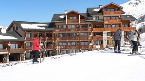 A multi-story wooden building with balconies, ski equipment, and a snowy mountain backdrop. - Bright apartment for 6, ski-in/ski-out, south terrace (Saint-Martin-de-Belleville)