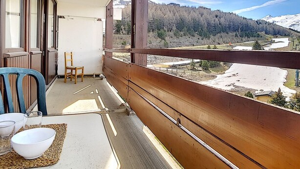 A balcony with a view of a mountainous landscape, a wooden railing, and a table with a bowl and glasses. - Bright apartment near slopes, balcony, pets allowed (Les Menuires)