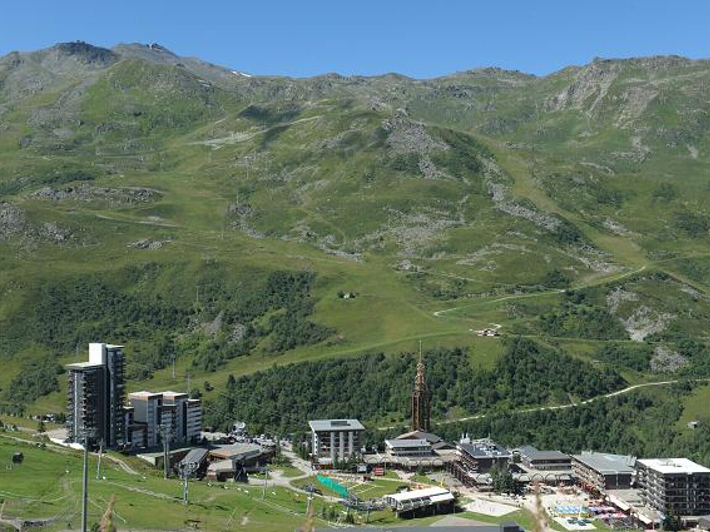 A mountainous landscape with a town featuring modern buildings, a swimming pool, and a ski lift.