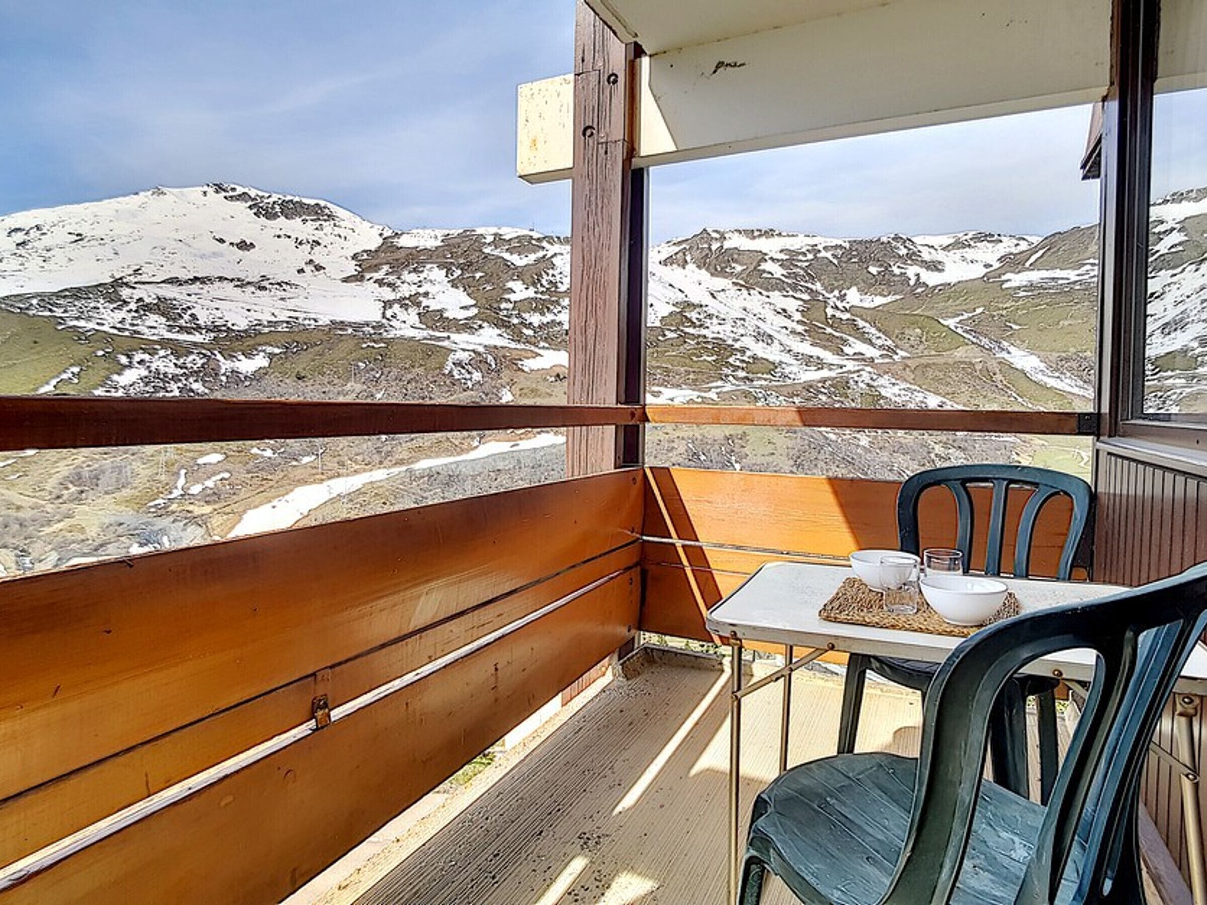 A balcony with a table and chairs, overlooking a mountainous landscape with snow.