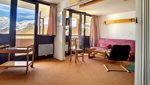 A cozy room with a sofa, a table, and chairs, large windows with curtains, and a view of mountains. - Bright apartment near slopes, balcony, pets allowed (Les Menuires)