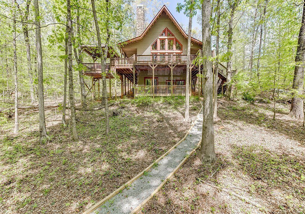 A cabin with a wooden deck and a covered porch, surrounded by a forest.