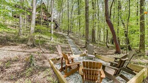 Skovområde med træterrasse, flere Adirondack-stole og en bygning i baggrunden.