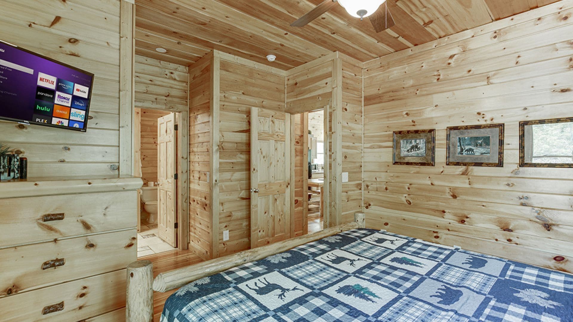 Habitación de una cabaña de madera con cama, televisor mostrando servicios de transmisión y fotografías enmarcadas en la pared.