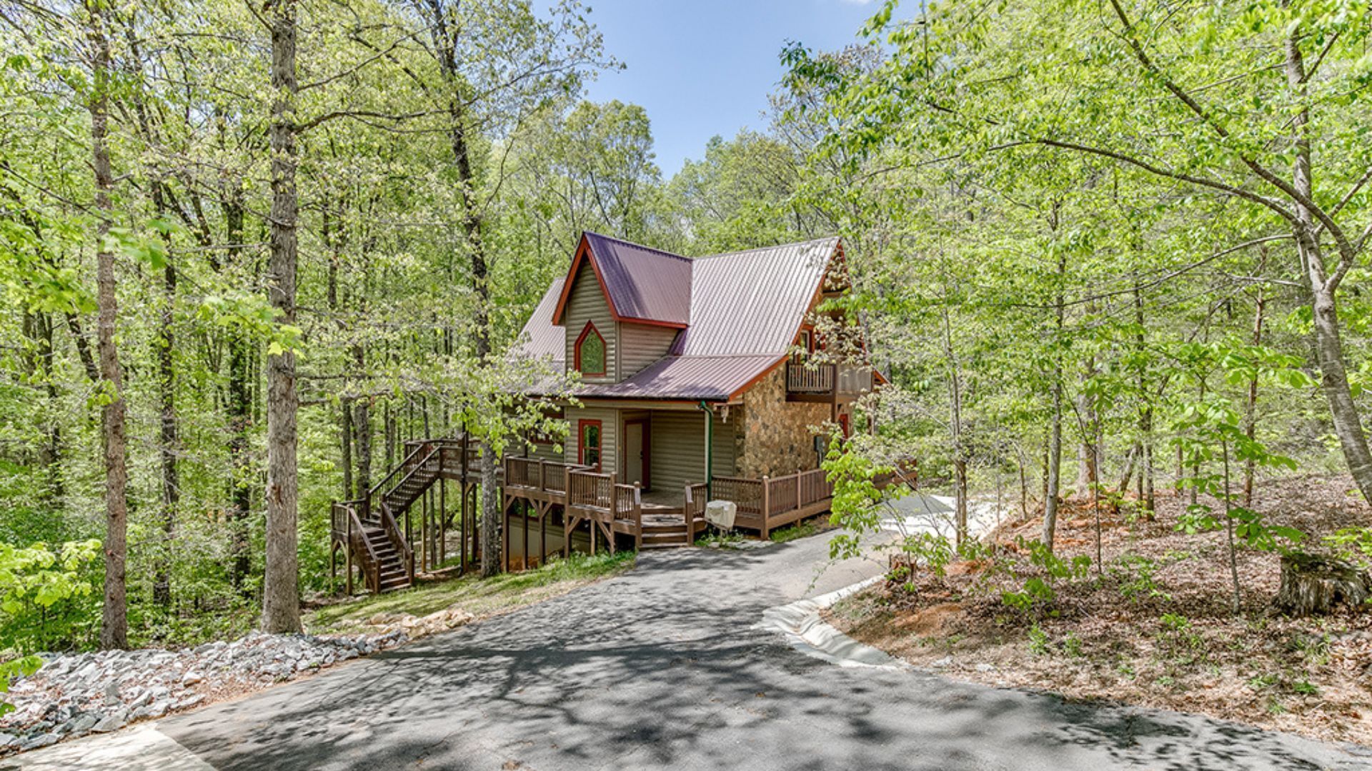 A cabin with a stone foundation, a metal roof, and a wooden deck.
