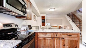 A kitchen with wooden cabinets, a microwave, and a stove. - Winterpoint 22: Breckenridge Townhome Near the Snowflake Lift (Breckenridge)