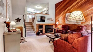 A spacious living room with a fireplace, a staircase leading to an upper level, and a cozy seating area with a lamp. - Winterpoint 22: Breckenridge Townhome Near the Snowflake Lift (Breckenridge)