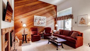 A living room with a wooden slat wall, red sofas, a coffee table, and a fireplace. - Winterpoint 22: Breckenridge Townhome Near the Snowflake Lift (Breckenridge)