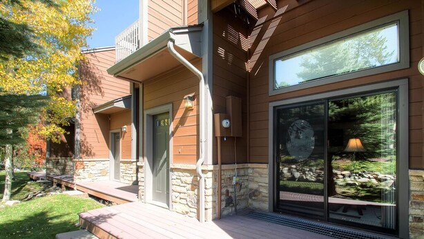 A modern house with a stone exterior, large sliding glass doors, and a deck with outdoor seating. - Winterpoint 22: Breckenridge Townhome Near the Snowflake Lift (Breckenridge)