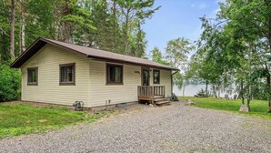 A single-story cabin with a front porch, a gravel driveway, and a lake view. - Sunrise Resort Northern Pike Cabin (Presque Isle)