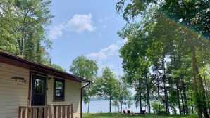 A cabin with a porch, a fishing-themed door, and a view of a lake surrounded by trees. - Sunrise Resort Northern Pike Cabin (Presque Isle)