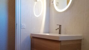 Ein Badezimmer mit einem weißen Waschbecken, einem Holz-Waschtisch und einem Spiegel mit Beleuchtung.
