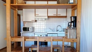 Eine kompakte Küche mit weißen Schränken, einer Mikrowelle, einem Spülbecken und einer Kaffeemaschine. Vier Holzstühle und ein kleiner Tisch sind vorhanden.