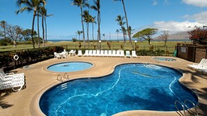 Una piscina con varias pistas, rodeada de sillas reclinables blancas y palmeras.