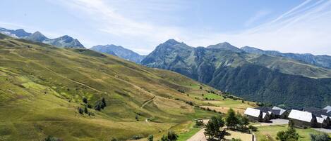 Ein ländliches Dorf mit traditionellen Häusern, einer asphaltierten Straße und einem Bergpanorama im Hintergrund.