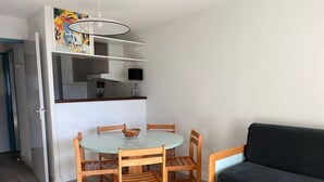 A compact living space with a round dining table, wooden chairs, a black sofa, and a kitchenette area.