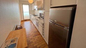 Eine kleine Küche mit einem Edelstahl-Kühlschrank, weißen Schränken und einem Holztisch.