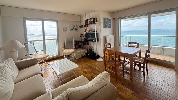 Ein Wohnzimmer mit einer Couch, einem Tisch, Stühlen, einem Fernseher und Meerblick durch große Fenster.