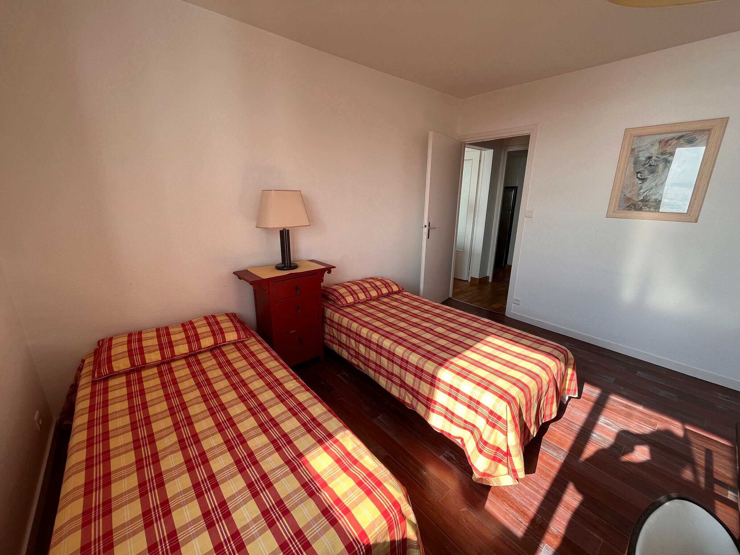 Une chambre avec deux lits, une table de chevet, une lampe et un tableau encadré au mur.