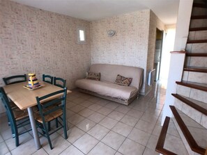 Ein Zimmer mit Fliesenboden, einer Couch, einem Tisch mit Stühlen und einem kleinen Fenster.