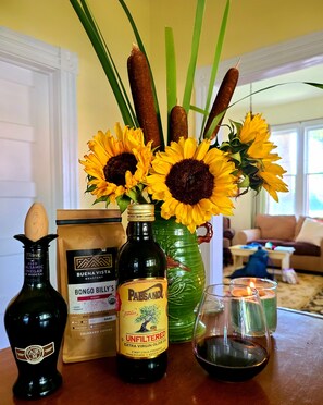 A table with a bottle of extra virgin olive oil, a bag of Bongo Billy's blend coffee, a bottle of Paesano, and a vase with sunflowers and green leaves. - Where Victorian Meets Cottage Farmhouse (Salida)