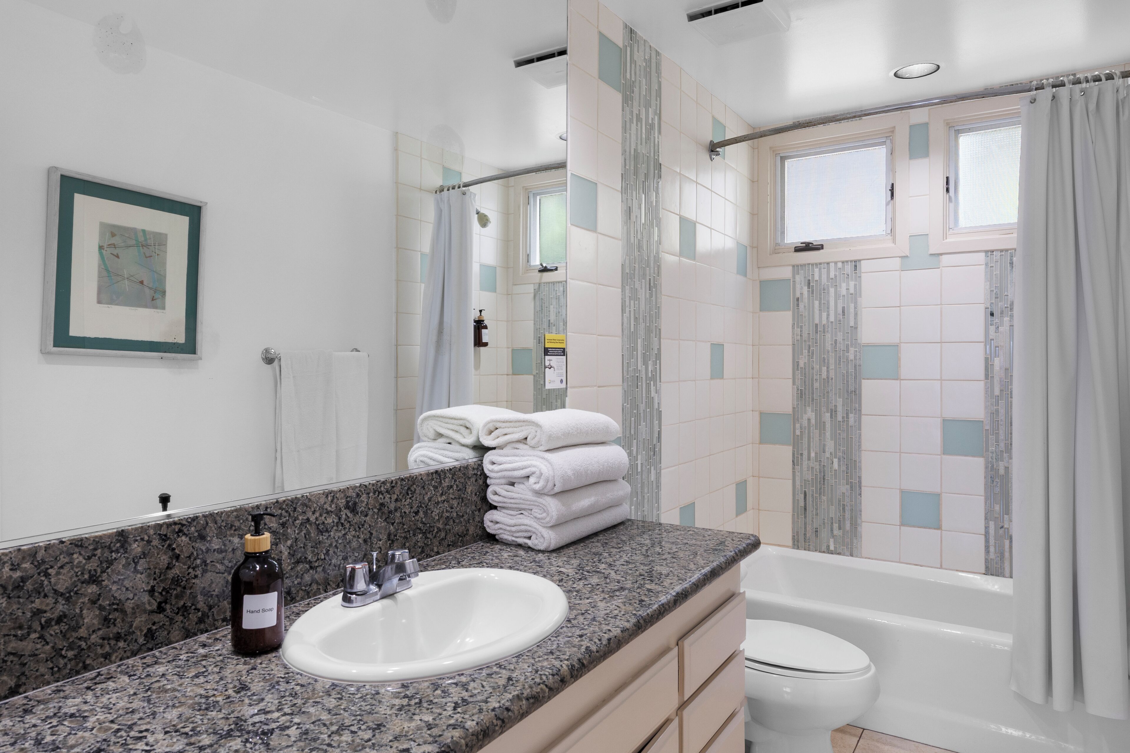 A modern bathroom with a granite countertop, white sink, and a bathtub.