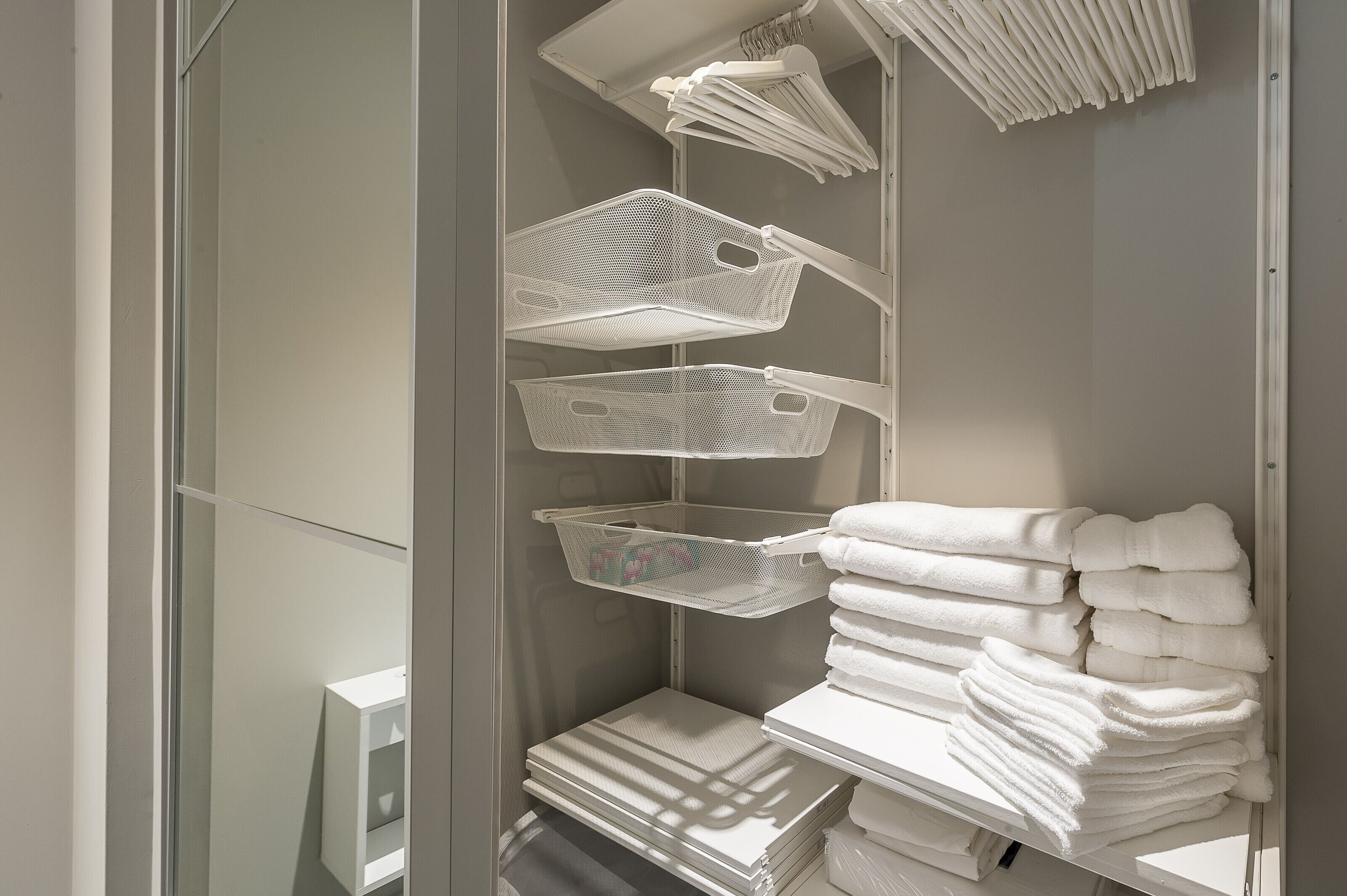 A storage area with shelves holding white towels and mesh baskets.