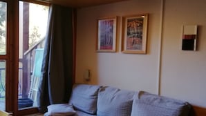 A room with a sofa, a table, and a window with curtains. There are two framed pictures on the wall.