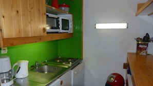 A compact kitchen with a microwave, kettle, and a red trash bin.