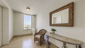 Une pièce comprenant un fauteuil en osier, une console, un grand miroir et une fenêtre donnant sur la ville.