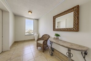 Une pièce comprenant un fauteuil en osier, une console, un grand miroir et une fenêtre donnant sur la ville.