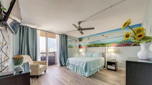 Une chambre à coucher comprenant un lit, une chaise, un bureau, un ventilateur de plafond, une table de chevet, une lampe et une fresque murale.