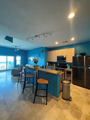 A modern kitchen with a central island, bar stools, a stainless steel refrigerator, and a microwave.