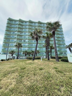 A multi-story hotel with balconies, surrounded by palm trees and a grassy area.