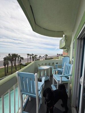 A balcony with a view of the beach, equipped with blue chairs and a small table.