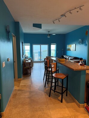 A kitchen with a bar area, a dining table, and chairs. There is a sliding glass door leading to a balcony.