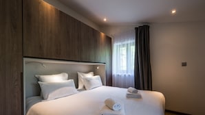 Un lit bien fait, avec des draps blancs et des serviettes pliées, une tête de lit en bois et une fenêtre avec des rideaux.