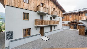 Un bâtiment moderne avec une façade en bois et des balcons, une cour recouverte de gravier et une enseigne indiquant la présence d’installations telles qu’un spa et une salle de sport.
