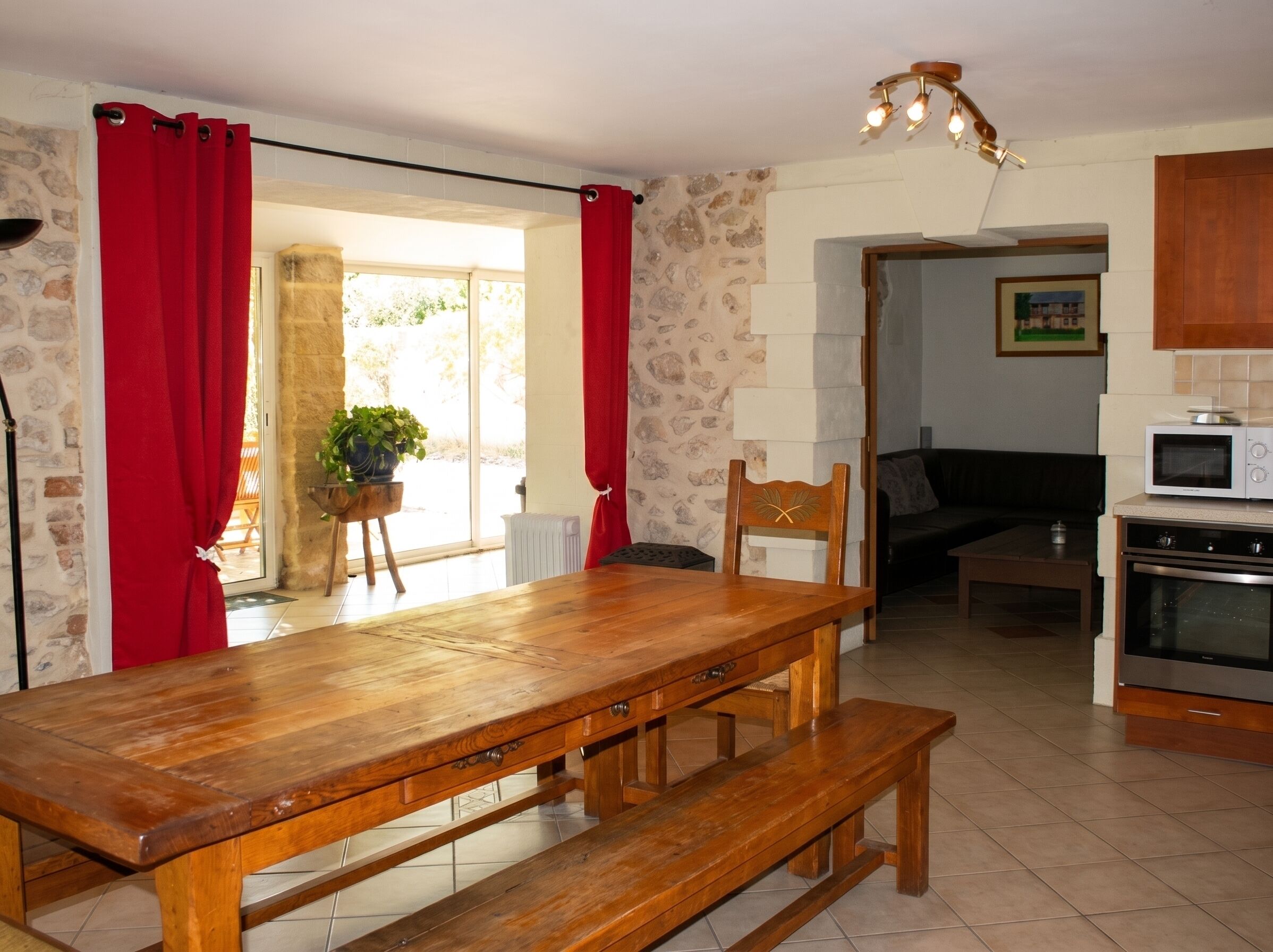 Une cuisine avec une table en bois, des rideaux rouges, une plante en pot, un four à micro-ondes et une cuisinière.